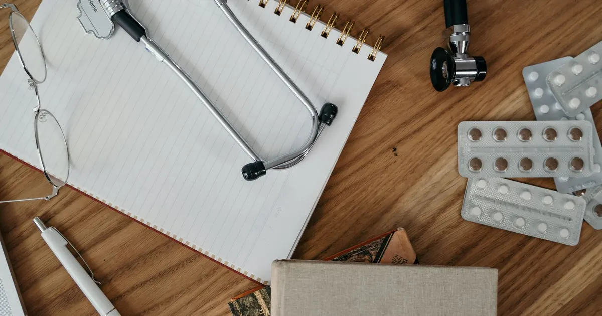 Stéthoscope posé sur un carnet vierge à côté de lunettes, vue de dessus sur un bureau en bois