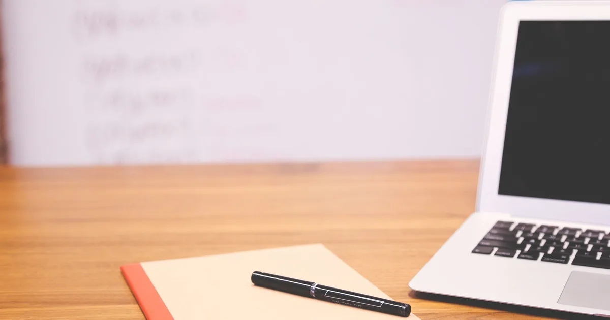 Stylo posé sur un carnet de notes, ordinateur portable flouté en arrière-plan, bureau professionnel