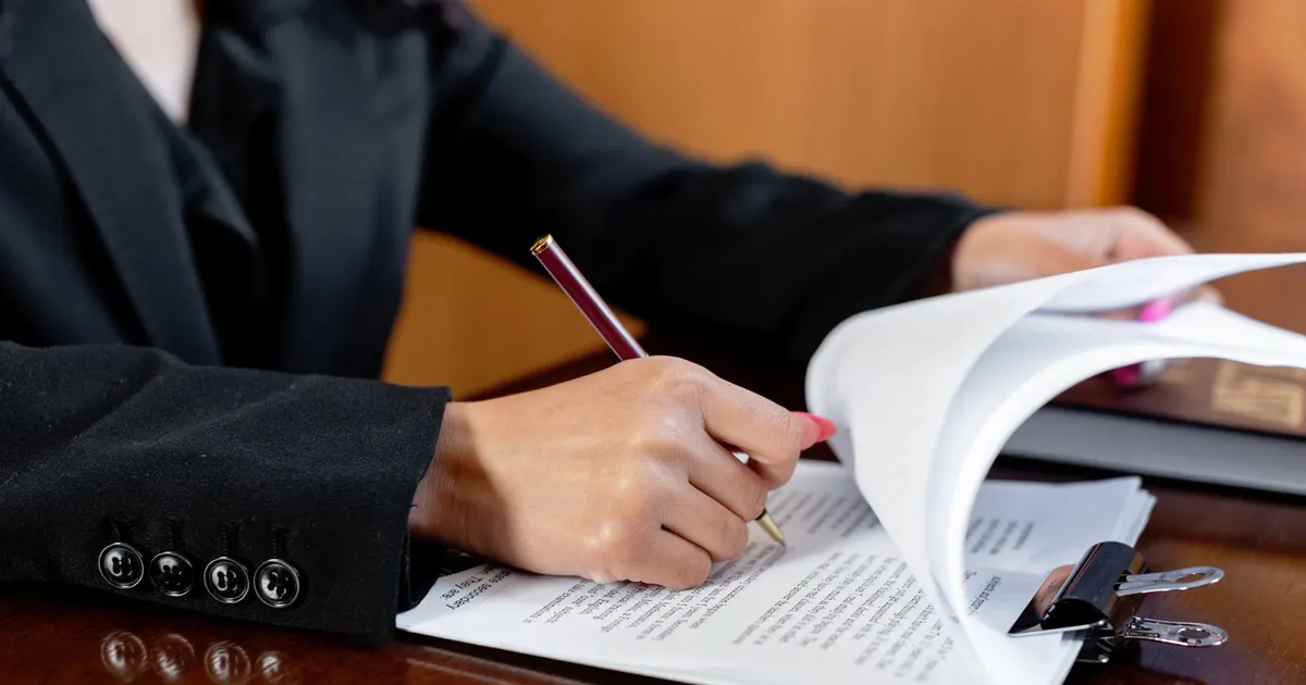 Avocat en robe noire annotant un document juridique sur un bureau en bois