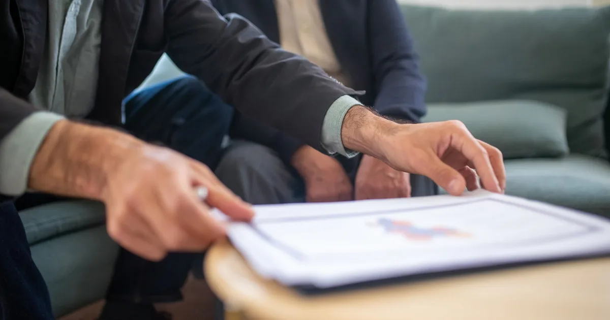 Mains désignant un document avec graphique lors d'un rendez-vous de conseil en assurance