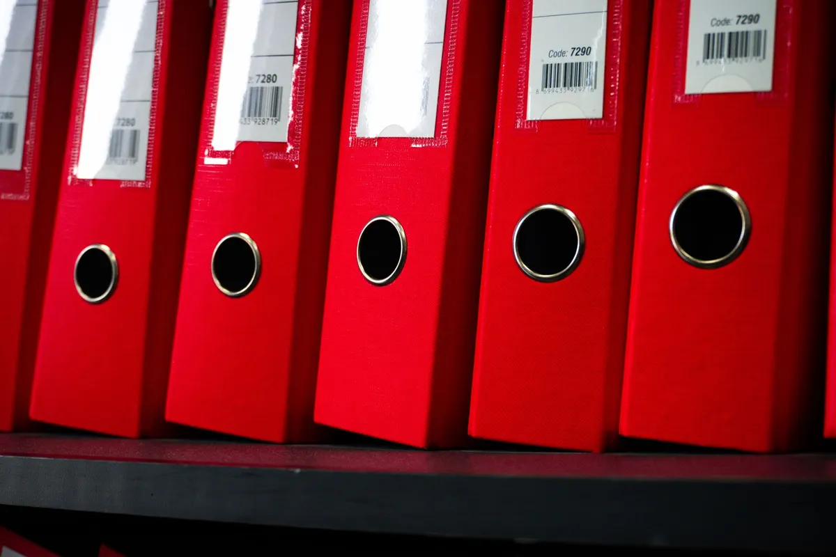 Rangée de classeurs d'archives sur une étagère, symbole des charges fixes et documents administratifs d'un cabinet