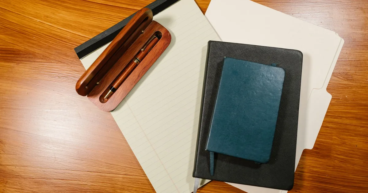 Stylo, bloc-notes et carnet posés sur un bureau en bois, symbole de la constitution d'un dossier administratif