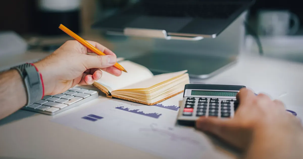 Professionnel libéral calculant ses cotisations et prestations de régime obligatoire avec calculatrice et carnet