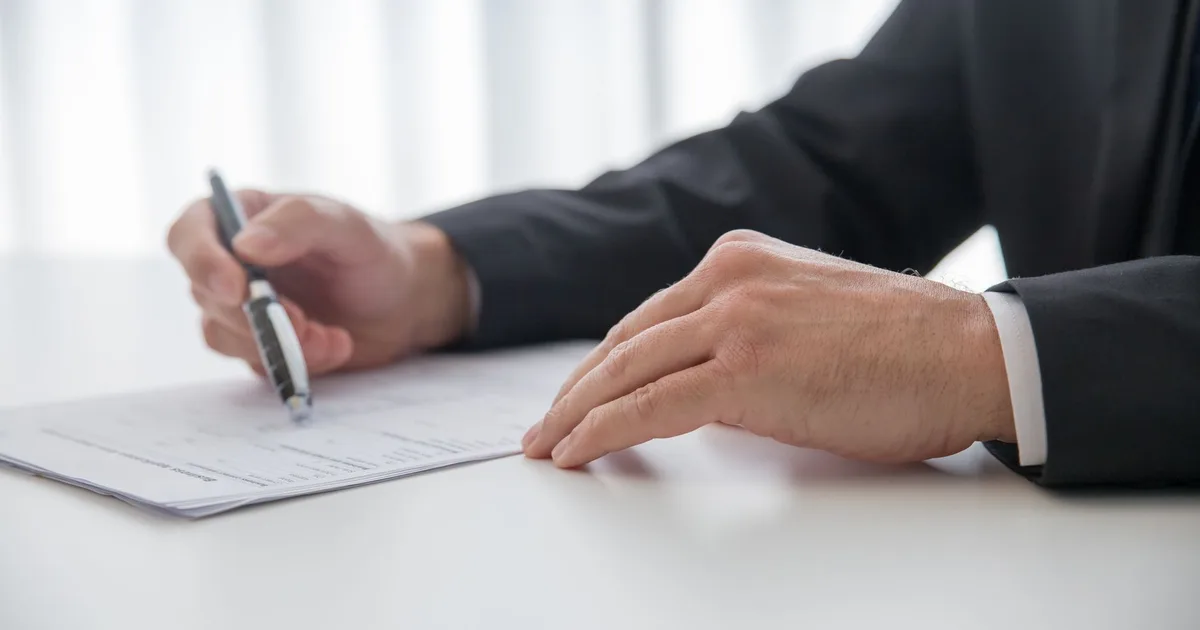 Mains signant un contrat avec un stylo sur un bureau, ambiance signature de document