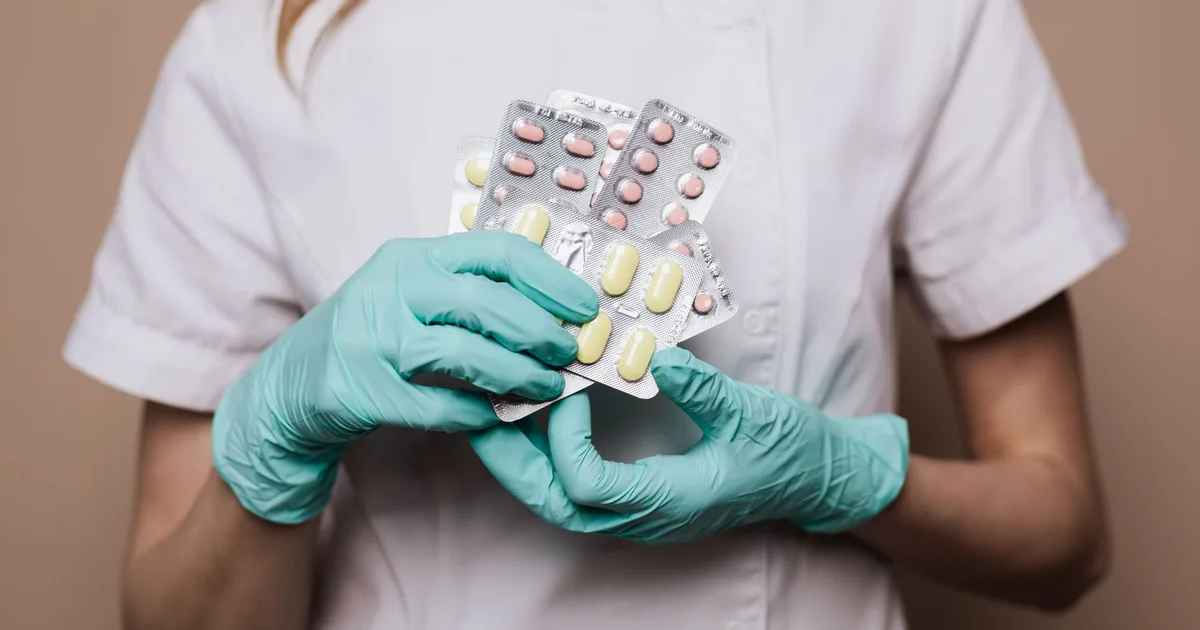 Mains gantées d'un pharmacien remplaçant tenant des plaquettes de médicaments